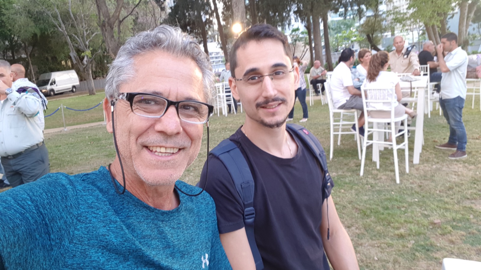 תמיר וגבר אפור שיער מחייכים בסלפי, באירוע על דשא.