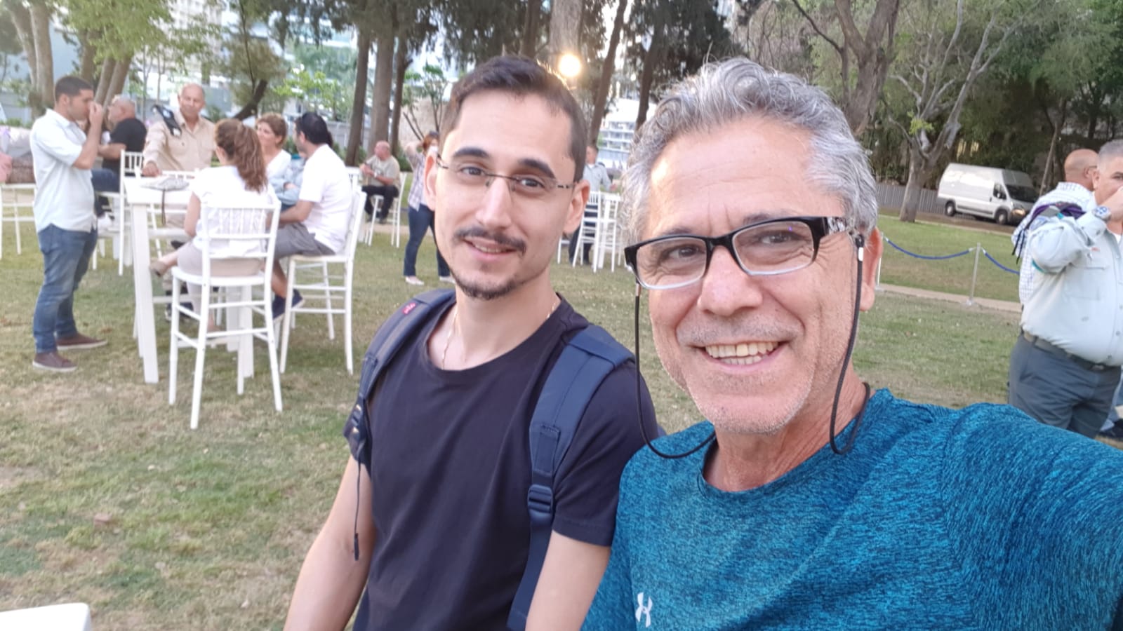 תמיר וגבר אפור שיער מצטלמים בסלפי באירוע על דשא, שניהם מחייכים.