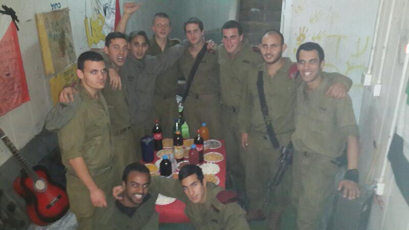 תמיר וחיילים נוספים במדים מצטלמים מחובקים סביב שולחן עם כיבוד.