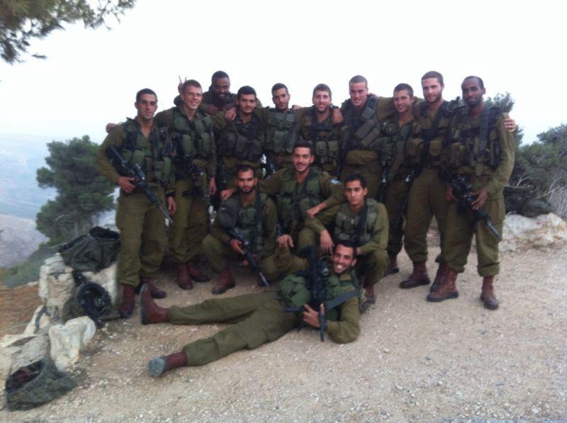 קבוצת חיילים במדים ובאפודים מצטלמת יחד על צלע הר, אחד מהם שוכב מלפנים.