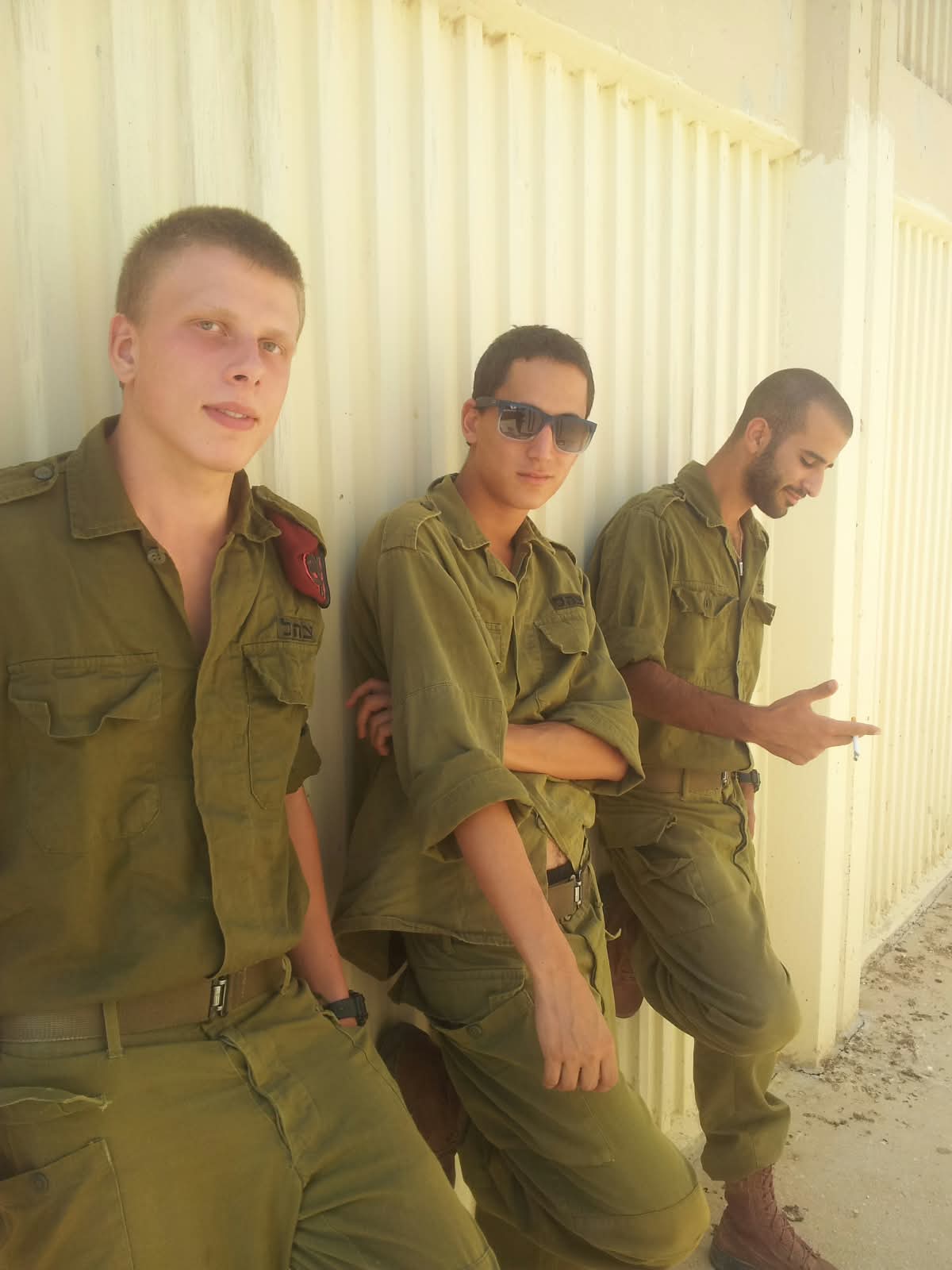 תמיר ושני חיילים נוספים במדים נשענים על קיר בהיר.